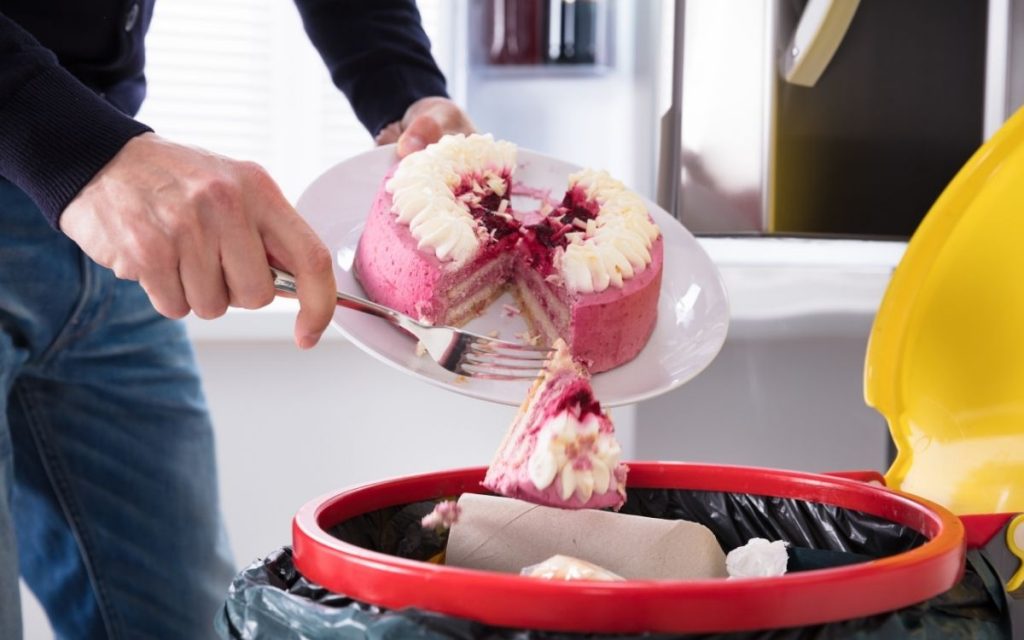 Person throwing a cake away into trash can