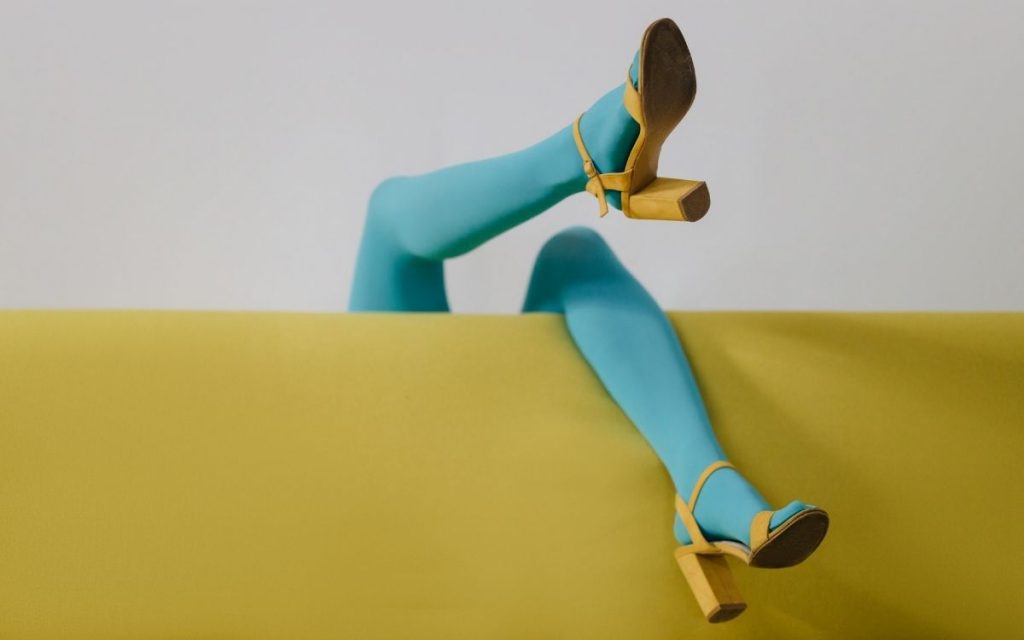 legs wearing blue leggings and yellow shoes dangle from the back of a couch