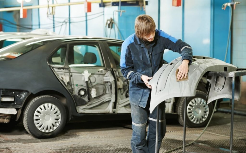 a man is sanding a plastic bumper in an auto repair shop 