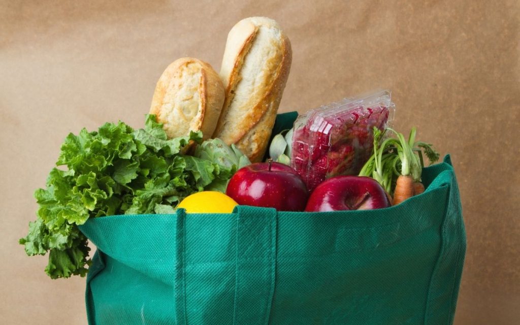 reusable grocery bag overflowing with fruits vegetables & bread